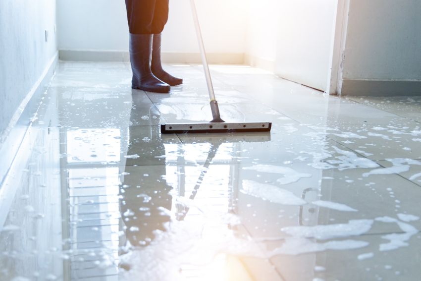 Cleaning worker mopping wet office floor with squeegee in hallway