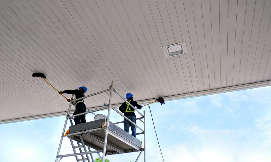 Two workers on scaffolding dusting a covered ceiling with long-handled dusters